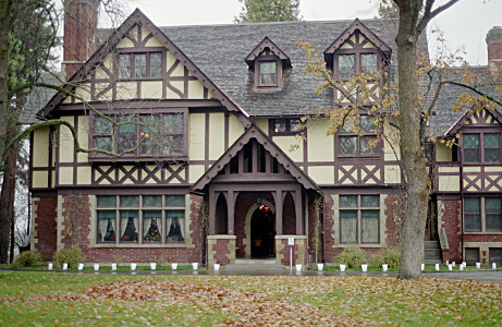 [A three story home with the first level brick and the upper levels are tan with dark brown wood x shapes and other decorations like is common on European Alpine homes.]